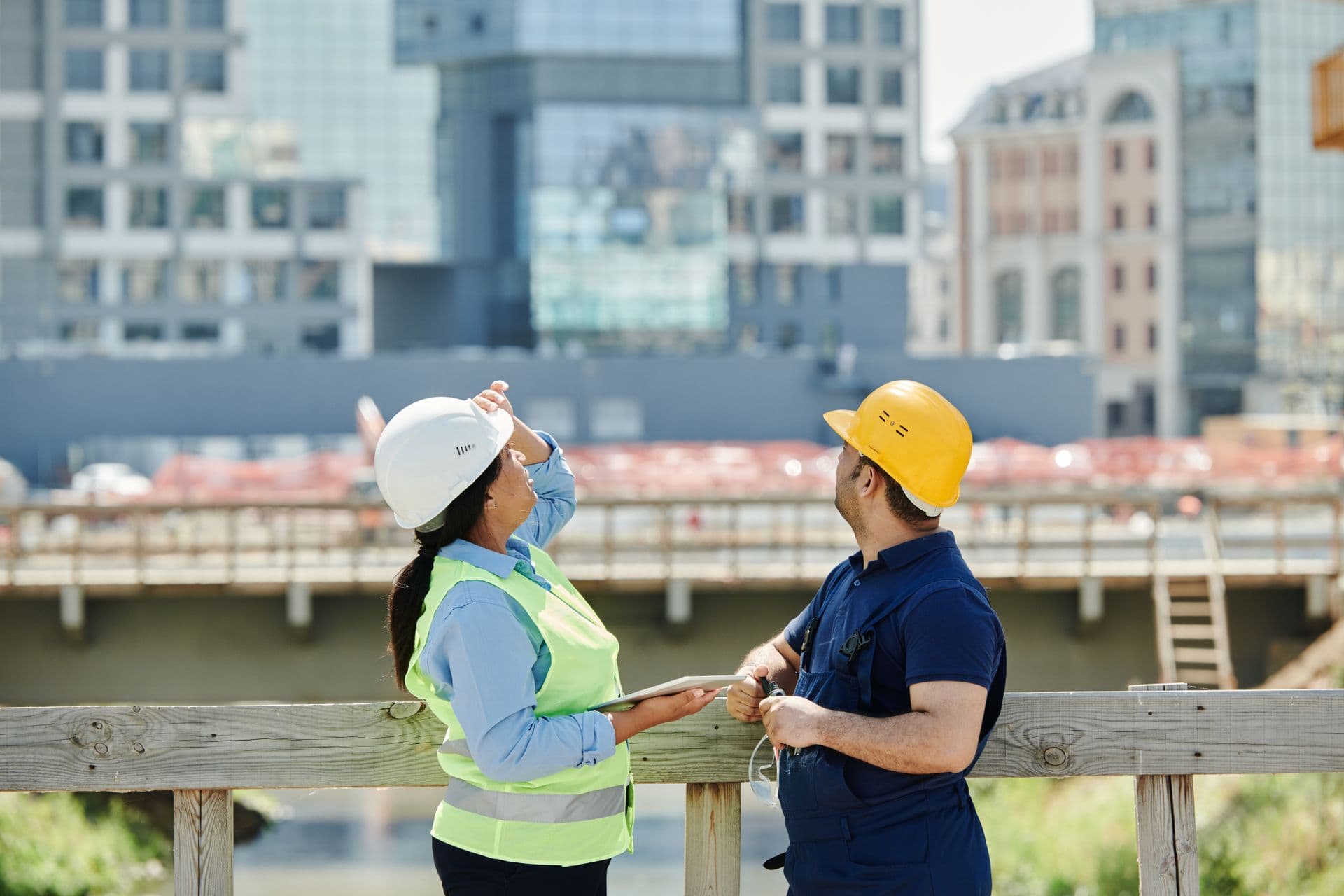 Two engineers in hard hats reviewing plans at a construction site.